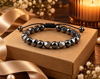 May include: A bracelet featuring alternating smooth and faceted dark gray metallic beads arranged in a circular pattern. The bracelet includes a black cord with an adjustable sliding knot closure and two small beads at the ends of the cord strings.