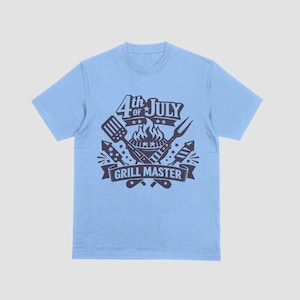 May include: Light blue t-shirt with a dark gray graphic. The graphic features the text "4th of July" above a grill with flames, a spatula, a fork, and fireworks. The text "GRILL MASTER" is below the grill.