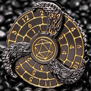 May include: A black and gold metal D&D dice spinner with a dragon design. The spinner features numbers and dice notations, including D4, D6, and D12. The center has a geometric shape.