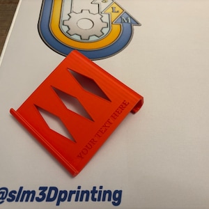 May include: A vibrant orange 3D-printed item featuring diamond-shaped cutouts and the text "YOUR TEXT HERE." It rests on a white surface, accompanied by a logo and the blue text "@slm3Dprinting".