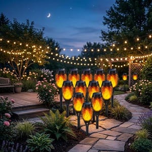 May include: A set of eleven black solar-powered garden torches arranged in a cluster, each featuring a realistic orange and yellow flame effect light, positioned on a stone pathway in a garden setting at night with string lights in the background.