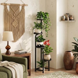 May include: A tall, black metal plant stand featuring five circular tiers arranged in a staggered, vertical design. The stand holds various potted plants, including a trailing vine, a red anthurium, and several green leafy plants in ceramic pots.
