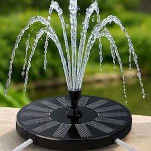 以下が含まれることがあります： 黒いソーラー噴水。水が噴き出すノズルを中心に、放射状のデザインが施された丸いベースがあります。水は優雅な弧を描き、ダイナミックなディスプレイを作り出しています。背景はぼやけており、屋外の環境を示唆しています。