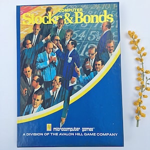 May include: A blue box with a yellow border and the text "COMPUTER Stock & Bonds" in white. The box features a colorful illustration of people in suits, with numbers and graphs in the background. The text "microcomputer games" and "A DIVISION OF THE AVALON HILL GAME COMPANY" is printed on the bottom of the box.