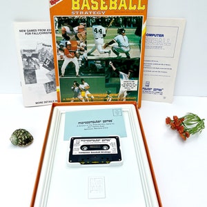 May include: A vintage box for a computer baseball strategy game. The box is orange and white with a picture of baseball players on the front. The game is from Microcomputer Games, a division of Avalon Hill Game Co. The box includes a cassette tape labeled "Computer Baseball Strategy".