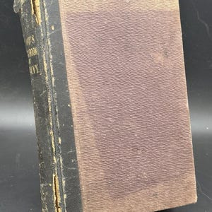 May include: An antique hardcover book with a textured brown cover and a black spine. The spine shows visible wear and fraying at the top and bottom edges. Faded gold lettering on the spine includes the words Handbook of Germany.