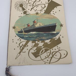 May include: Vintage travel brochure featuring a detailed illustration of the SS United States ocean liner sailing on blue waters. The cover has gold decorative elements and a tassel. The brochure is bound with a brown cord.