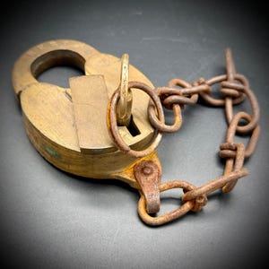 May include: An antique brass padlock with a key and a rusty chain. The padlock has a heart-shaped design with the word "LIBERTY" embossed on the top. The chain is made of rusty metal links.