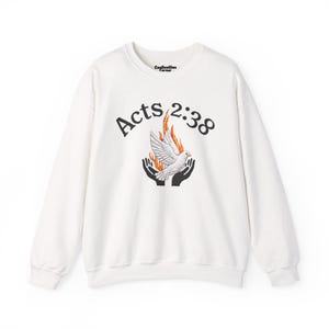 Op de afbeelding: Witte crewneck sweatshirt met de tekst "Acts 2:38" boven een afbeelding van een witte duif, vlammen en handen. De duif staat in het midden van het ontwerp, met vlammen die erachter oprijzen. De sweatshirt heeft lange mouwen.