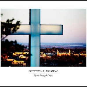 May include: A photograph of a large, white cross in the foreground, with a city skyline and sunset in the background. The text "FAYETTEVILLE, ARKANSAS" and "Mount Sequoyah Cross" is at the bottom.