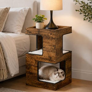 May include: A two-tier wooden cat house side table with a dark brown wood grain finish and black metal frame accents. The top surface holds a lamp and a small potted plant, while the lower level contains a white cushion with a resting cat.