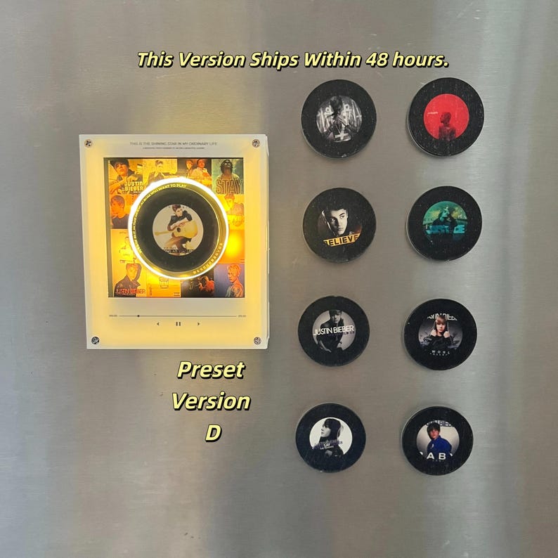May include: A square, illuminated display frame featuring a central circular graphic, accompanied by eight smaller, circular black magnets. The display shows a grid of images and a playback interface. The text reads "This Version Ships Within 48 hours." and "Preset Version D".