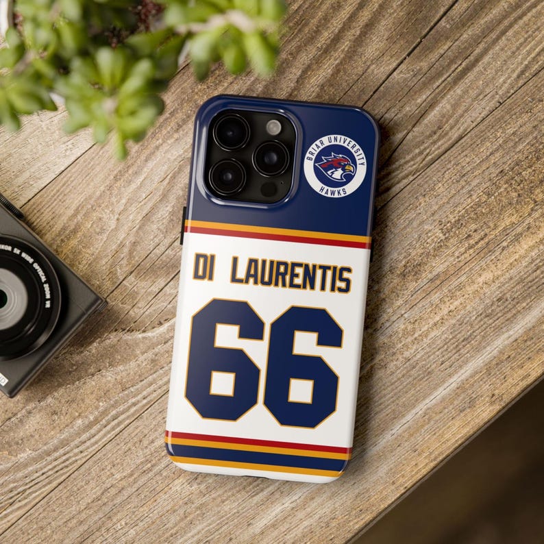 May include: A phone case with a navy blue top section featuring a Briar University Hawks logo. The lower section is white with the name "DI LAURENTIS" and the number "66" in navy blue. The case has a red and gold stripe design.