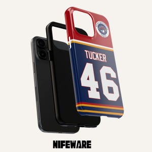 May include: A phone case with a jersey design. The case is navy blue with the name "Tucker" and the number "46" in white. The top is red with a team logo. The phone and case are black. The word "NIFEWARE" is at the bottom.