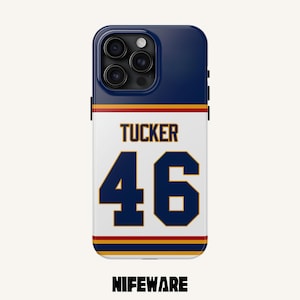 K&ouml;nnte beinhalten: Eine marineblaue und wei&szlig;e Handyh&uuml;lle mit dem Namen "Tucker" und der Nummer "46" in Marineblau und Gold. Die H&uuml;lle hat eine marineblaue Oberseite und den Markennamen "NIFEWARE" unten.