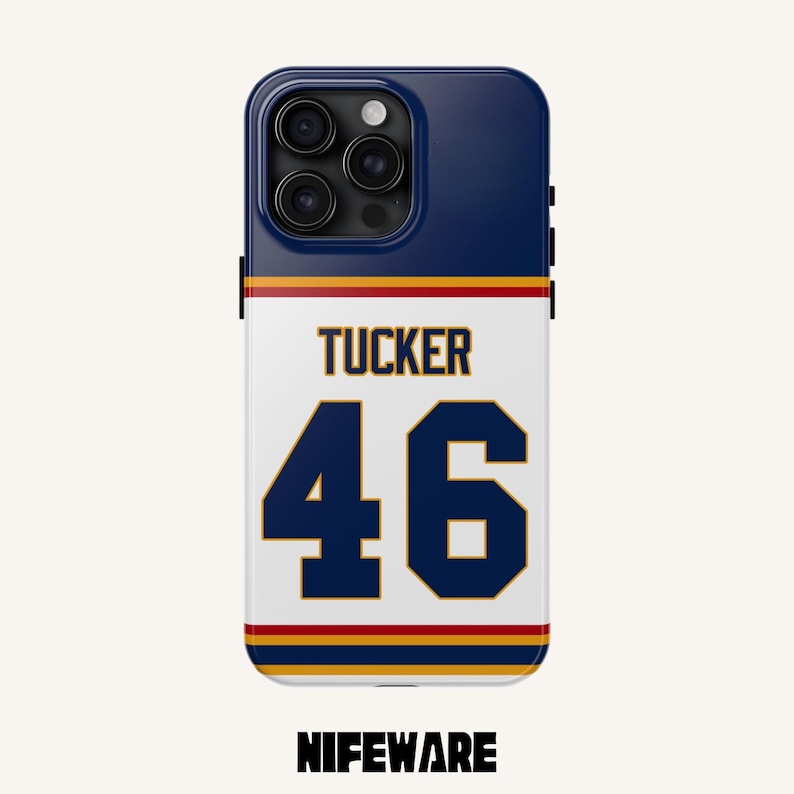K&ouml;nnte beinhalten: Eine marineblaue und wei&szlig;e Handyh&uuml;lle mit dem Namen "Tucker" und der Nummer "46" in Marineblau und Gold. Die H&uuml;lle hat eine marineblaue Oberseite und den Markennamen "NIFEWARE" unten.