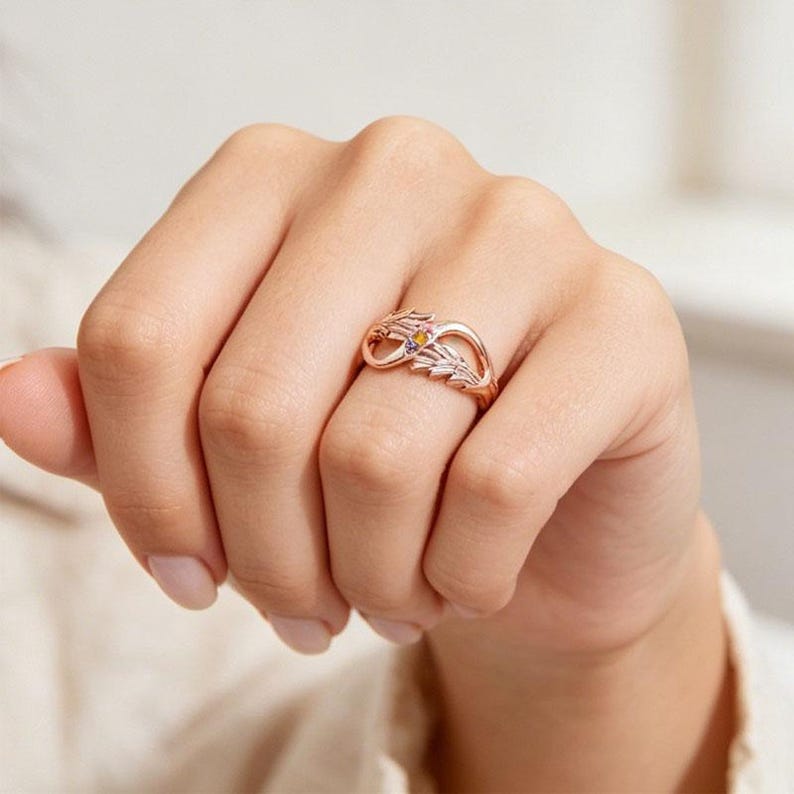 May include: Rose gold ring featuring a delicate leaf design with small, colorful gemstones. The ring is worn on a hand, showcasing its intricate details and elegant style. A unique piece of jewelry.