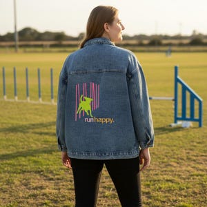 May include: A denim jacket with a neon green dog graphic and the words "run happy" in yellow. The graphic is set against a pink striped background. The jacket is a medium wash denim.