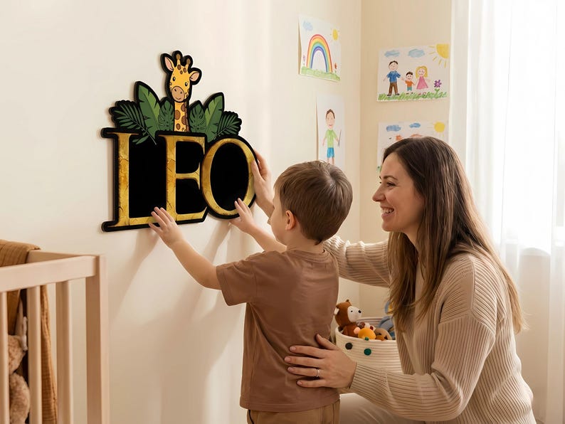 May include: A wooden wall decoration spelling out the name "LEO" in gold lettering. The letters are set against a black background, with a giraffe and green leaves above. A child and an adult are shown interacting with the decoration.