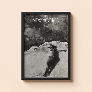 Op de afbeelding: Een zwart-wit ingelijste muurkunstprint met de tekst THE NEW YORKER bovenaan. De afbeelding toont een persoon in een bikini met stippen liggend op een rotsachtig oppervlak bij water, vastgelegd in een contrastrijke vintage-stijl foto.