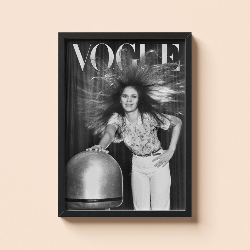 Puede incluir: Impresi&oacute;n enmarcada en blanco y negro de una portada de la revista Vogue. La portada presenta a una mujer con el pelo peinado hacia arriba, vestida con una camisa floral y pantalones blancos. El logo de Vogue est&aacute; en la parte superior. La mujer se apoya en un objeto grande, met&aacute;lico y redondeado.