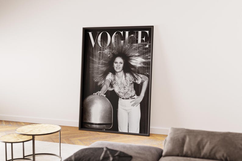 Puede incluir: Portada de la revista Vogue enmarcada en blanco y negro. La imagen muestra a una mujer con el pelo peinado hacia arriba. El logo de Vogue est&aacute; en la parte superior. La mujer lleva una camisa floral y pantalones blancos. El marco est&aacute; apoyado en una pared blanca.