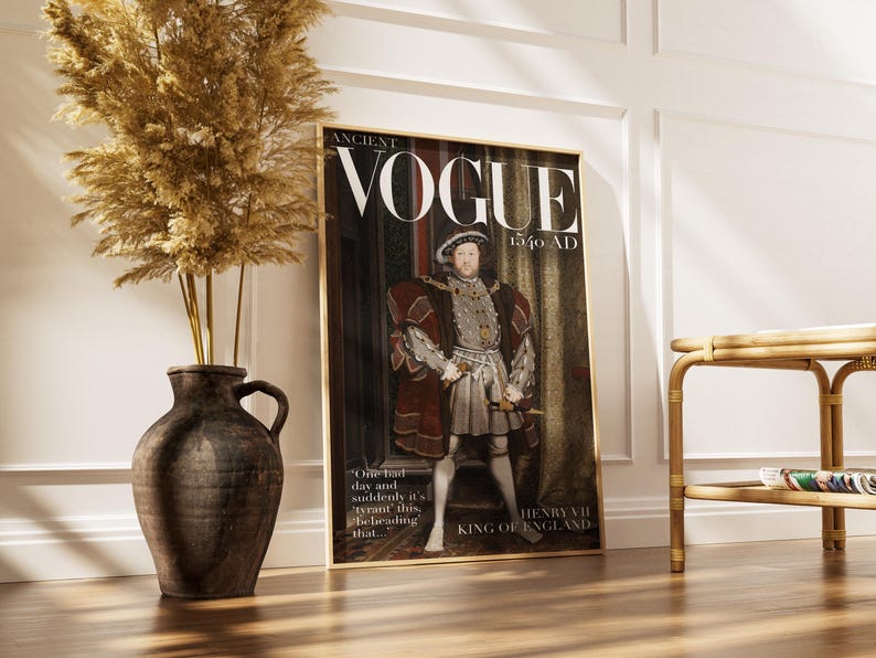 May include: A framed print of a magazine cover titled "ANCIENT VOGUE 1540 AD" featuring a portrait of King Henry VII of England. The print is in a gold frame and is propped against a white wall. A large brown vase with dried plants is to the left.