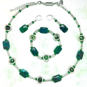 Könnte beinhalten: Ein Schmuckset mit Halskette, Armband und Ohrringen. Das Set umfasst eine silberfarbene Kette mit rechteckigen und ovalen Steinen in Grün und Türkis. Die Ohrringe haben ein passendes Design. Das Armband hat ein ähnliches Design.