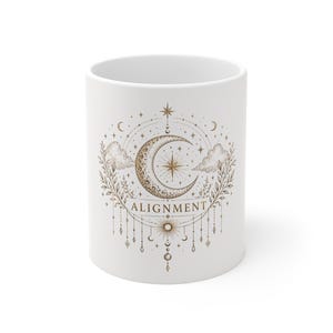 Pode incluir: Caneca de cerâmica branca com um design celestial, apresentando uma lua crescente, estrelas e a palavra "ALIGNMENT" em uma fonte decorativa. O design é em tons de ouro e marrom, com um estilo artístico. A caneca tem um formato cilíndrico padrão.