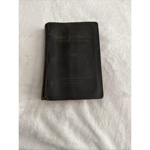Puede incluir: Un manual negro vintage titulado "Manual de Instrucción Ingeniería de Clientes" con el logotipo de IBM. El manual está desgastado, con pliegues y desgaste visibles en la cubierta. También es visible el texto "International Business Machines Corporation".