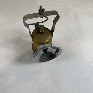 Op de afbeelding: Een vintage koperen carbid mijnwerkerslamp met een gepolijste chromen reflector, een cilindrisch koperen brandstofreservoir en een stevige metalen draagbeugel aan de bovenkant. De lamp is voorzien van een kleine schroefdop en een brandermondstuk.