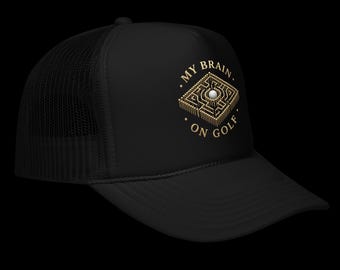 Puede incluir: Gorra de camionero negra con parte trasera de malla y visera curva. La gorra presenta un diseño cuadrado dorado con un laberinto y una pelota de golf, y el texto "MY BRAIN ON GOLF" en dorado.