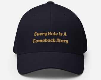 Puede incluir: Gorra de béisbol azul marino con el texto dorado "Every Hole Is A Comeback Story". La gorra tiene una visera curva y un ajuste estructurado, adecuada para diversas actividades al aire libre.