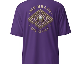 Puede incluir: Una camiseta morada de manga corta con un gráfico en la espalda. El diseño muestra un laberinto cuadrado construido con tees de golf de madera con una pelota de golf blanca en el centro. El texto "MY BRAIN ON GOLF" está impreso en dorado alrededor.