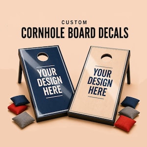 May include: Two cornhole boards with black frames and glossy surfaces, one dark blue and one light wood-grain, both featuring the text "YOUR DESIGN HERE" in dark blue. Includes six bean bags in red, blue, and gray, with "CUSTOM CORNHOLE BOARD DECALS" text.