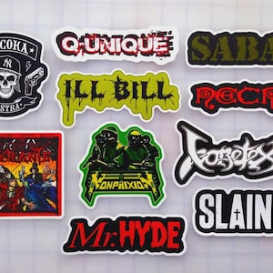 May include: A white ceramic mug with a black handle and the text "But First, Coffee" in a black, handwritten-style font. The mug is on a white surface.