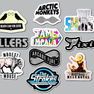 May include: A selection of music band stickers, including "Death Cab for Cutie," "Tame Impala," and "The Strokes." The stickers are in various shapes and sizes, with a gray background. The stickers are ideal for decorating items.