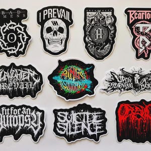 Pode incluir: Uma coleção de autocolantes de logótipos de bandas a preto e branco, com vários designs e texto. Os autocolantes incluem logótipos de bandas como "Bad Omens", "I Prevail" e "Architects". Alguns autocolantes têm toques de cor.