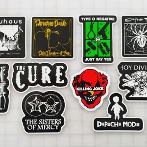 May include: A selection of stickers displaying logos and artwork from bands such as Bauhaus, Christian Death, Type O Negative, Cocteau Twins, Siouxsie and the Banshees, The Cure, Joy Division, Killing Joke, The Sisters of Mercy, and Depeche Mode.