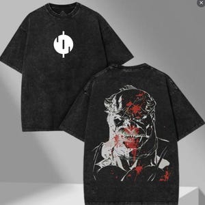 May include: Two black t-shirts. One has a white graphic on the front, and the other features a detailed illustration on the back with red accents. The shirts have a washed, textured appearance.