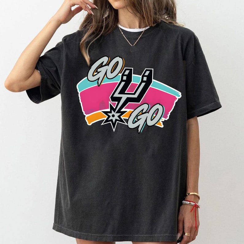 May include: Dark grey t-shirt with a colourful graphic reading "GO 4 GO". The design includes a lightning bolt, starburst, and a teal, pink, and orange colour scheme. The shirt has a casual, oversized fit.