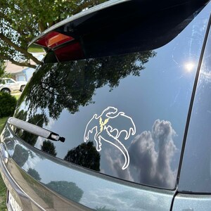 May include: A green car with a white dragon sticker on the back window. The dragon is flying with its wings spread out.