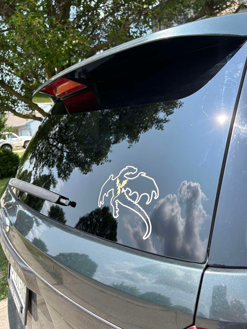 May include: A green car with a white dragon sticker on the back window. The dragon is flying with its wings spread out.
