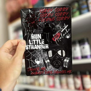 May include: Black rectangular sticker with a gas mask graphic, spiderwebs, and the text "RUN LITTLE STRANGER". Additional text includes "Sorry", "property of Malachi", and "Choose Nobody". Red and white accents.