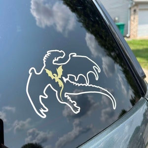 May include: A white vinyl sticker of a dragon silhouette with a smaller dragon silhouette inside. The sticker is on a black car window.