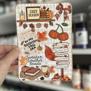 May include: A rectangular sticker with a cozy autumn theme. It features illustrations of pumpkins, books, leaves, and a coffee cup. Text includes "Cozy Season," "In My Bookish Fall Era," and "Sweater Weather Reads."