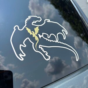 May include: A white silhouette of a dragon with a smaller gold dragon inside, on a black car window.
