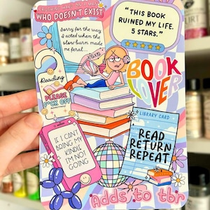 May include: A colorful sticker with a book lover theme. The sticker features a cartoon illustration of a person reading, a pink phone, and the text "This book ruined my life. 5 stars." and "Adds to tbr".