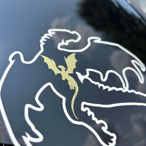 May include: A white outline of a dragon with a gold dragon inside. The dragon is on a black surface.