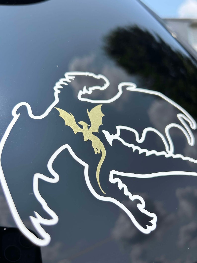 May include: A white outline of a dragon with a gold dragon inside. The dragon is on a black surface.